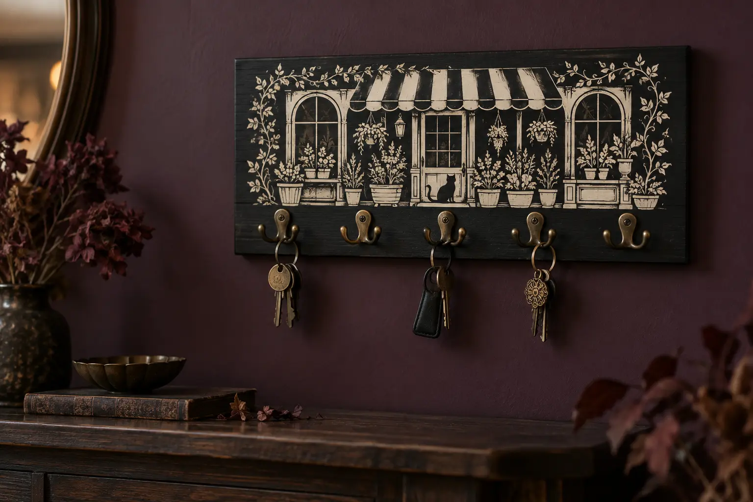 Finished matte-black wooden entryway key holder with a cream haunted flower-shop vinyl scene, five antique-brass hooks, and three lightweight key rings